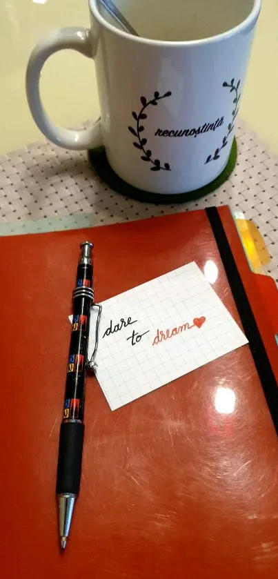 Orange notebook with pen and inspirational card beside a mug.