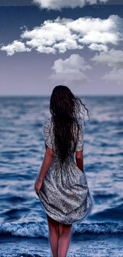 Woman stands facing ocean under cloudy moonlit sky.