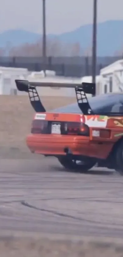 Red sports car drifting on a track with mountains in the background.