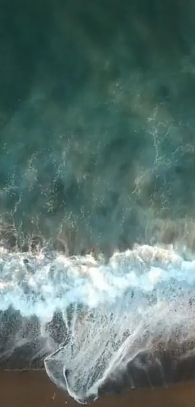 Aerial view of ocean waves crashing onto a sandy shore, featuring vivid teal water.