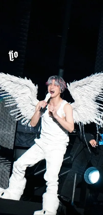 Performer with angel wings on stage, holding a microphone.