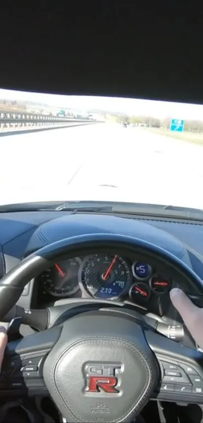 Car steering wheel and dashboard view from a driver’s perspective on the highway.