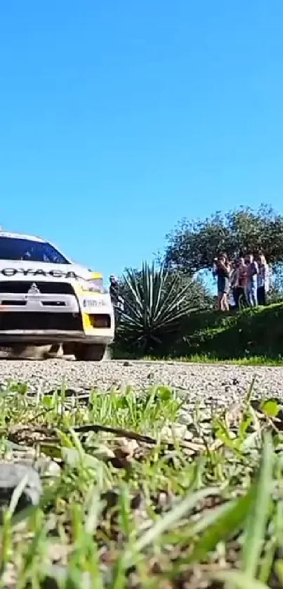 Rally car speeding on a gravel road under a clear blue sky.