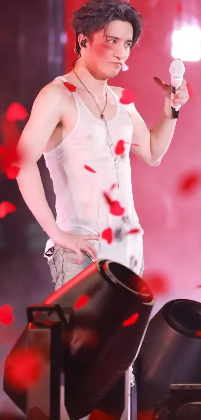 Performer on stage with red lighting and petals, holding a microphone.