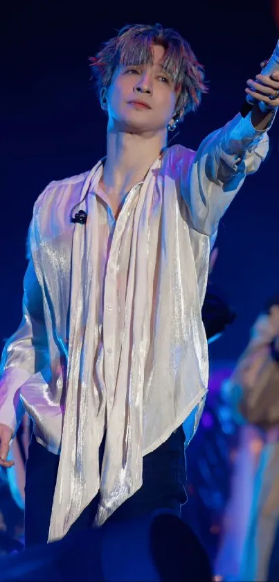 Performer on stage holding microphone with vibrant blue lighting.