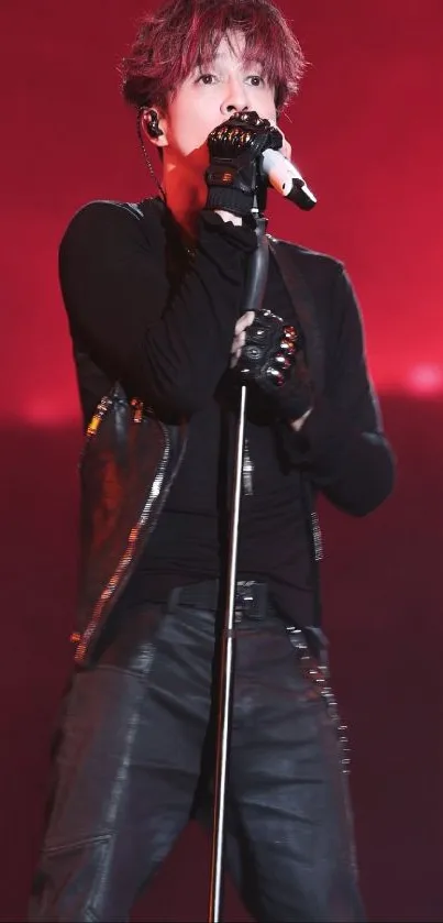 Performer in black outfit singing on a red-lit stage.