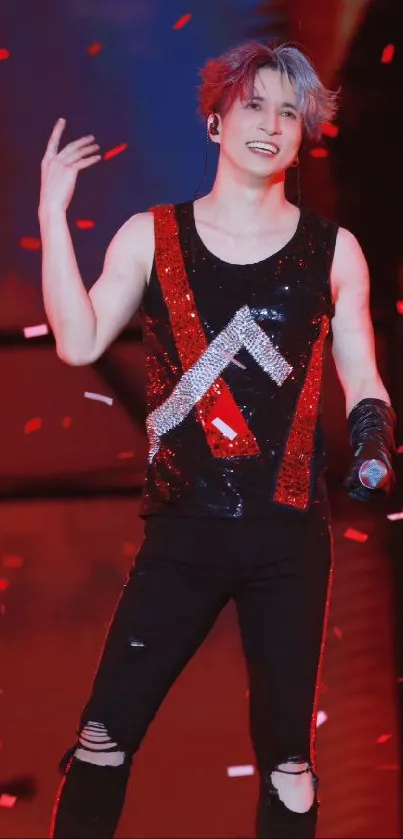 Energetic performer in glittery outfit on concert stage with vibrant red lights.