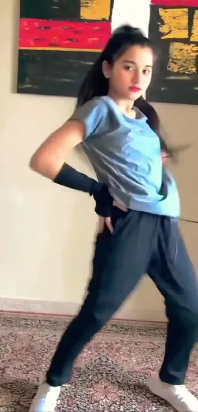 Person in blue shirt and pants striking a dance pose indoors.