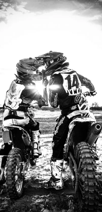 Two dirt bikers in black and white, facing each other with helmets on a sunny dirt track.