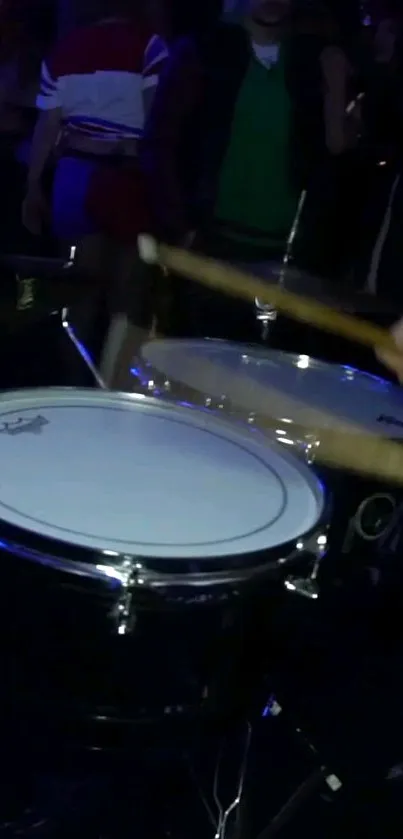 Close-up of drumsticks hitting drums in a dark, lively scene.