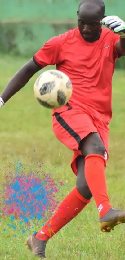 Goalkeeper in red kicking soccer ball on green field.