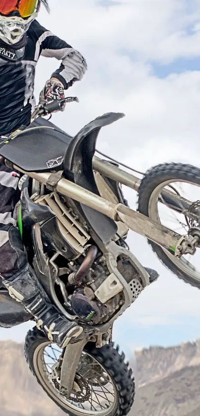 Motocross rider jumps high against a rugged mountain backdrop.