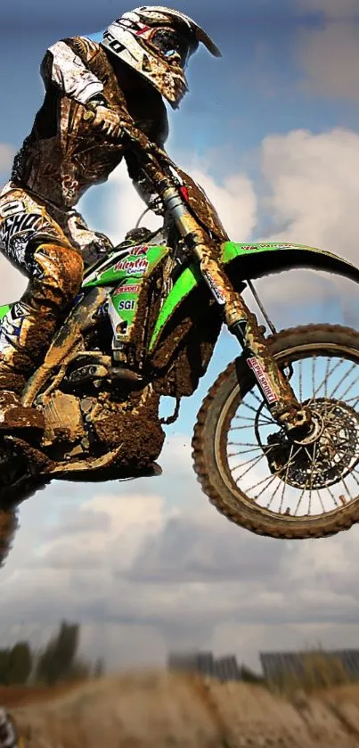 Motocross rider jumping with muddy bike under cloudy sky.