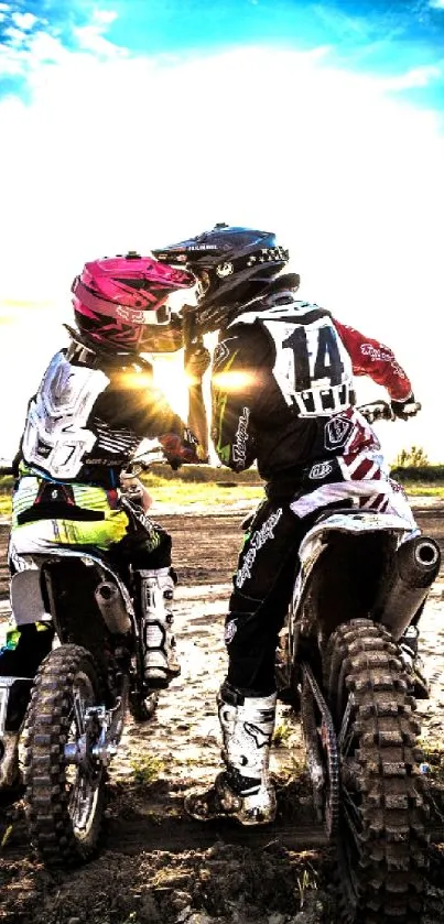 Motocross riders embrace during sunset.