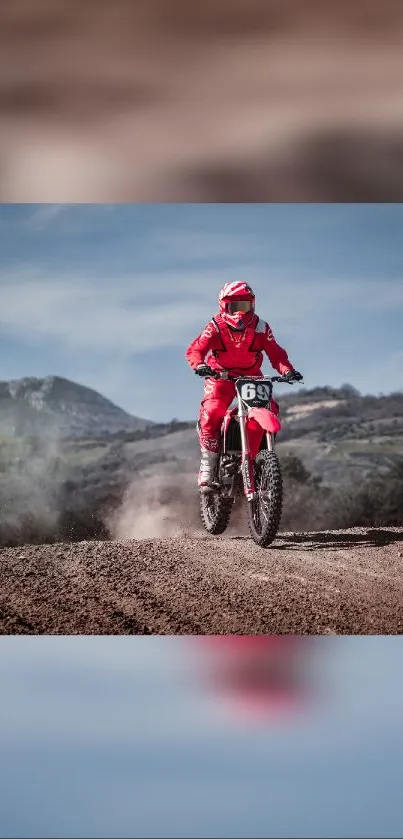 Motocross rider in red gear on dirt track with mountains in background.