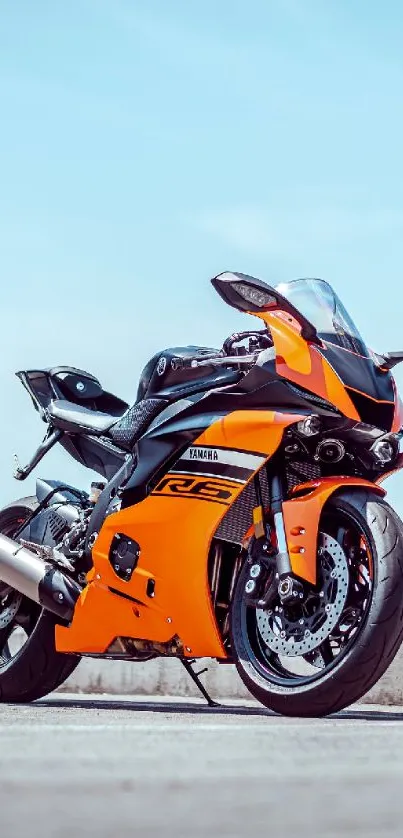 Vibrant orange sport motorcycle on urban road with clear sky.