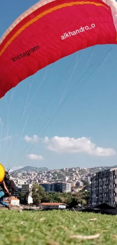 Vibrant red paraglider over cityscape under blue sky.