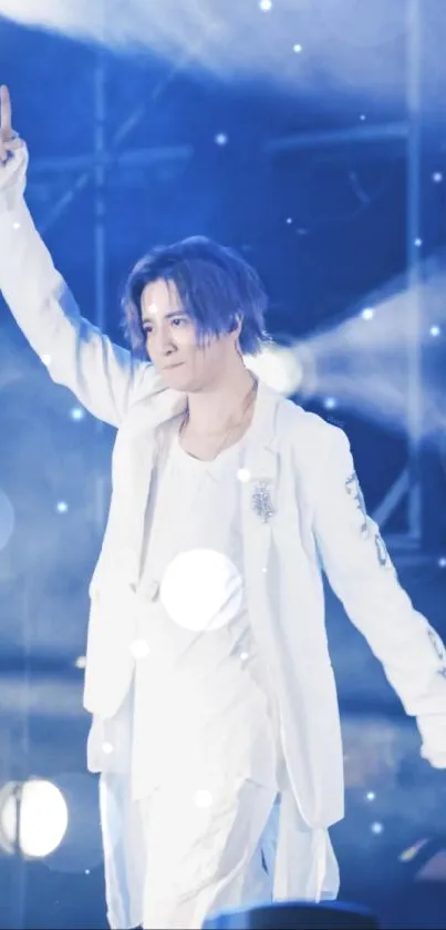 Performer on stage in blue lighting with white attire and raised hand.