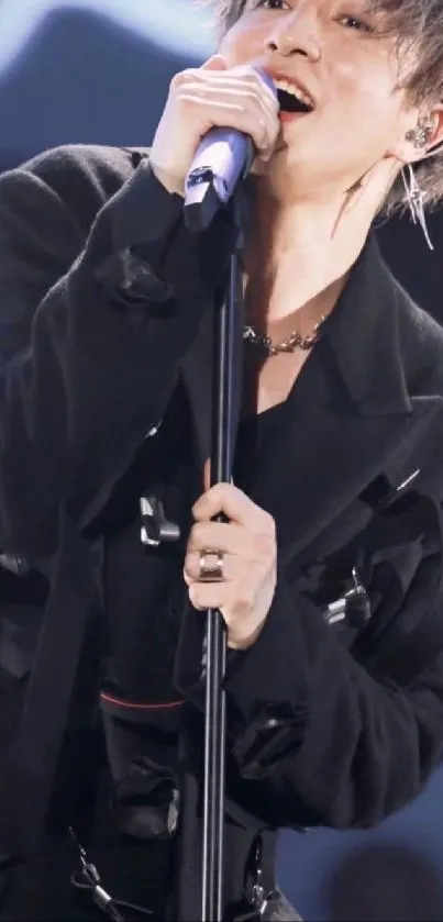 Singer passionately performing live on stage, gripping microphone and wearing black outfit.