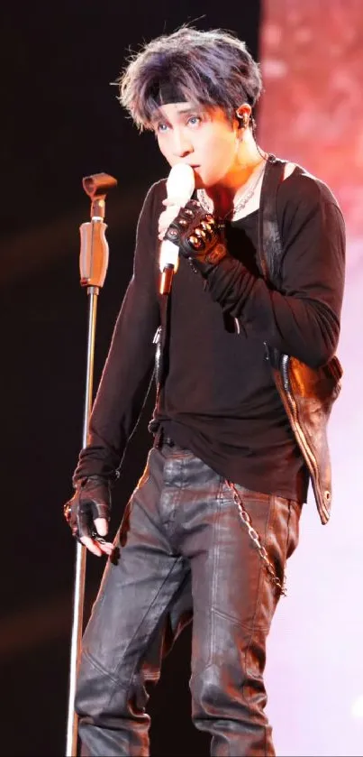 Performer on stage in black outfit with microphone.