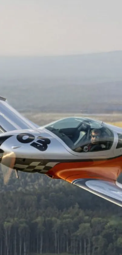 Orange plane flying over forested landscape in gray tones.