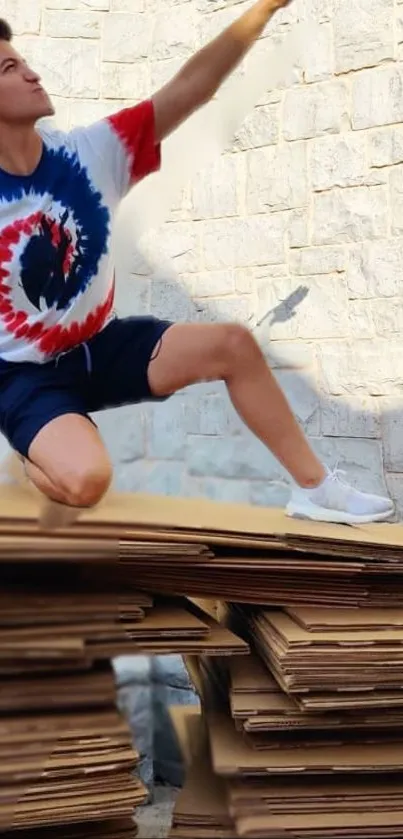 Person striking a dynamic pose on cardboard stacks against a stone wall.