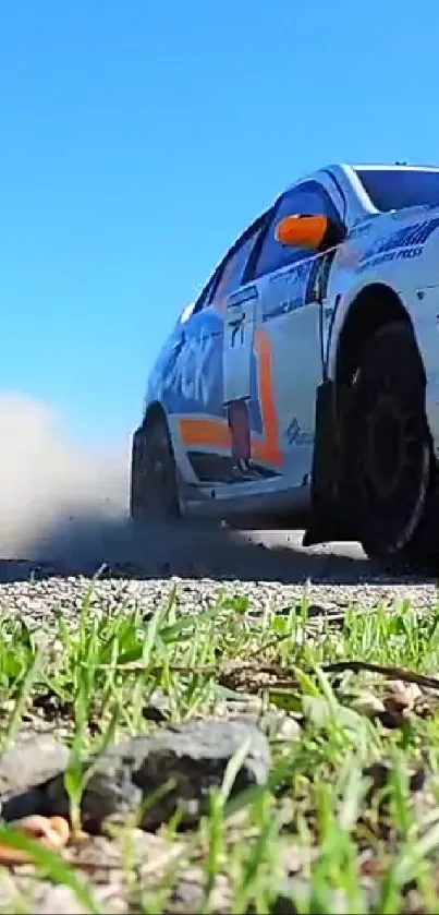 Rally car speeding on gravel with blue sky backdrop and green grass.