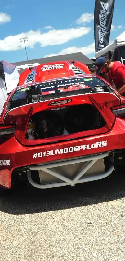 Red race car parked with open trunk at a racetrack event.