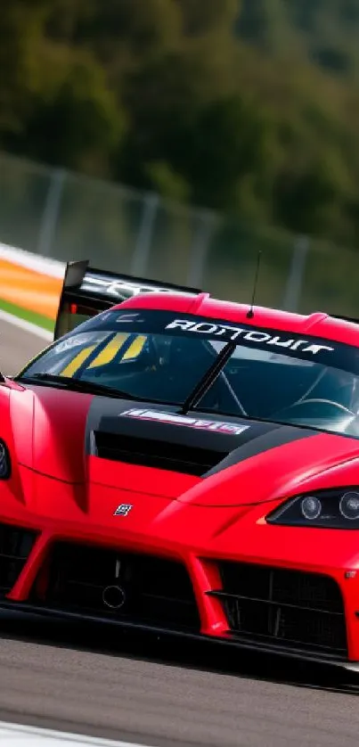 Red sports car speeding on racetrack with forest backdrop.