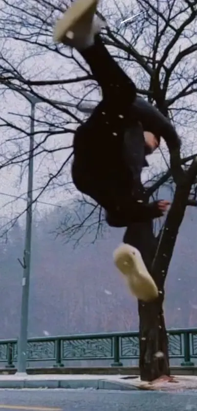 Acrobatic jump in snowy urban landscape with leafless tree.