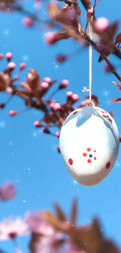 Easter egg hanging on a blossoming branch with a blue sky background.