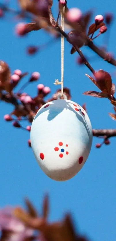 Easter egg hanging on a spring branch with blue sky background.