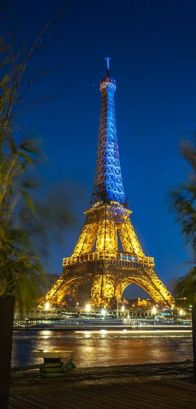 Eiffel Tower glowing at night, framed by plants against a blue sky.