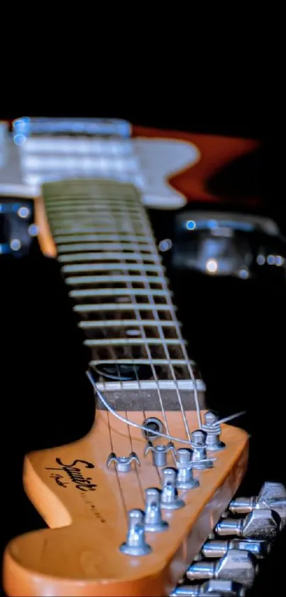 Close-up of an electric guitar neck with strings against a black background.