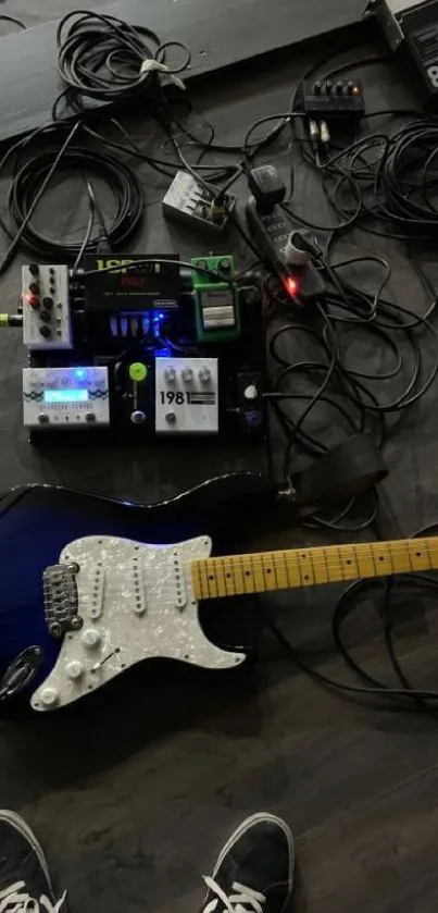 Electric guitar with effects pedals on dark floor.