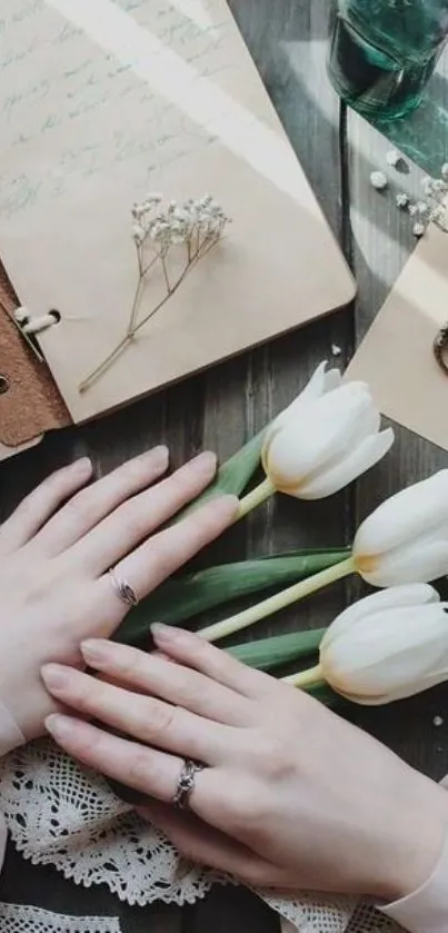 Hands holding white tulips on a rustic wooden table with vintage notebooks.