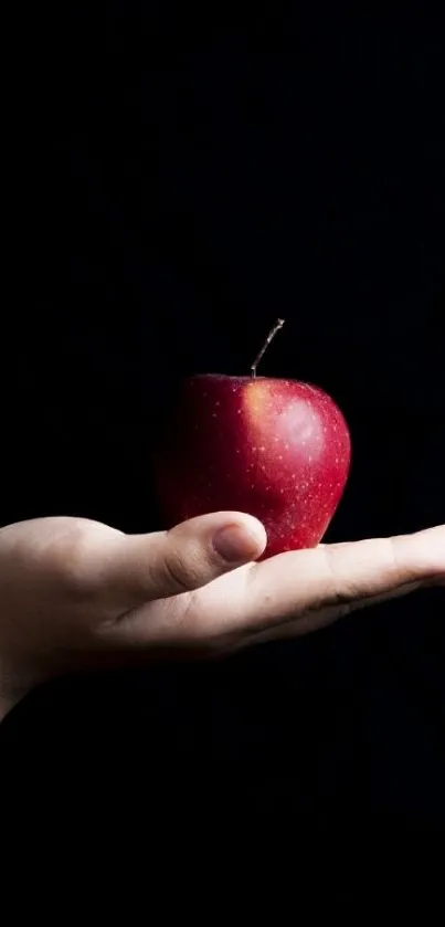 Hand holds a red apple on a black background.