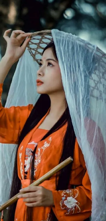 Asian woman in orange dress with veiled hat in serene forest.