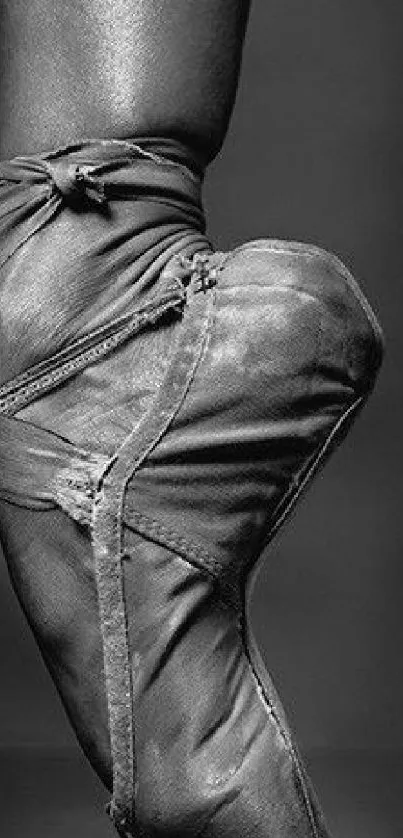 Close-up of a foot in a worn ballet pointe shoe in black and white.