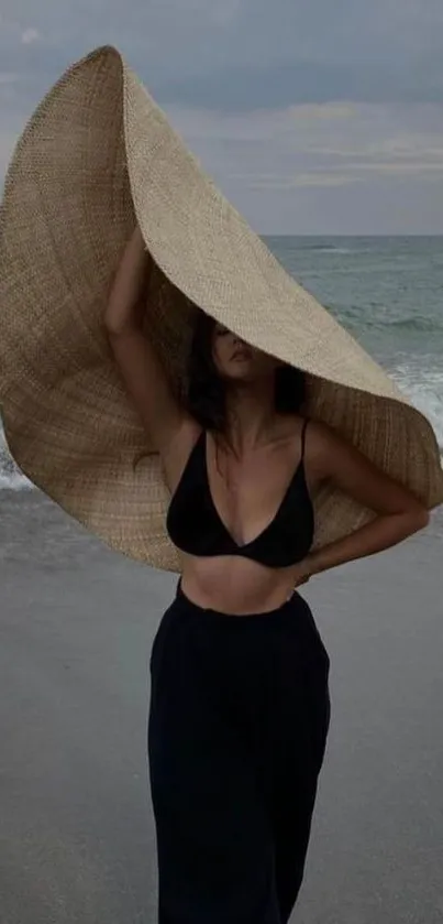 Elegant woman with large sun hat on beach near ocean.