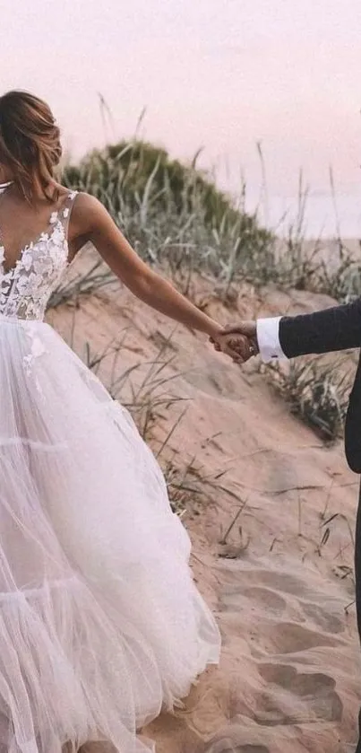 Bride and groom holding hands on a sandy beach at sunset.