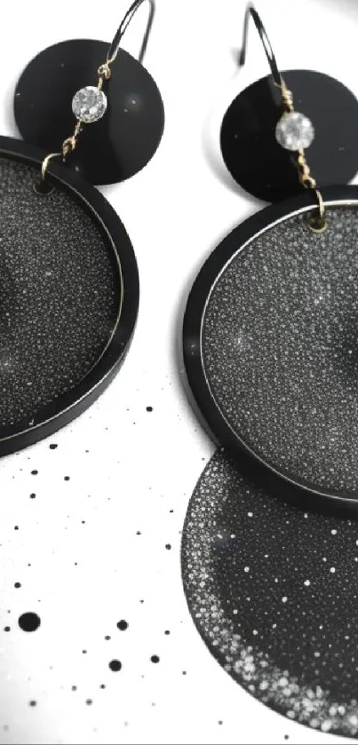 Elegant black earrings with cosmic design on wallpaper.