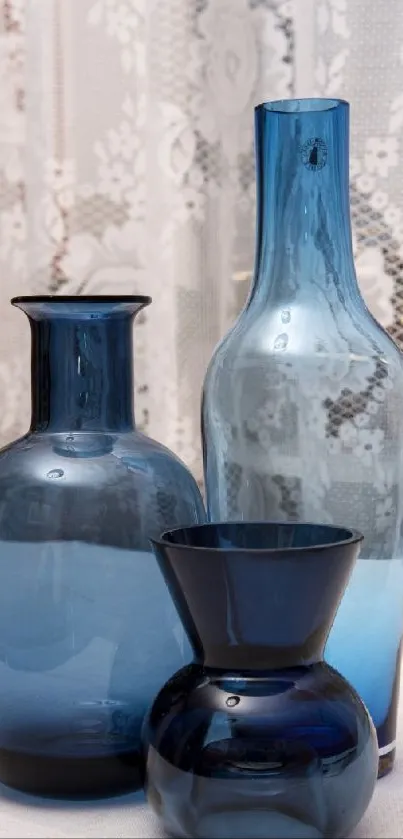 Elegant arrangement of blue glass vases with lace backdrop.