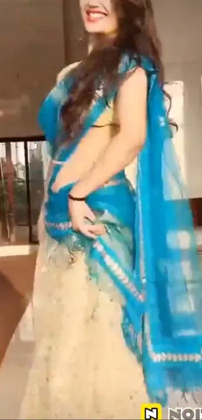 Woman in blue saree standing elegantly in sunlight, indoors.