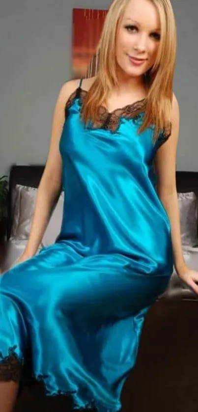 Woman in elegant blue satin dress sitting on a bed.