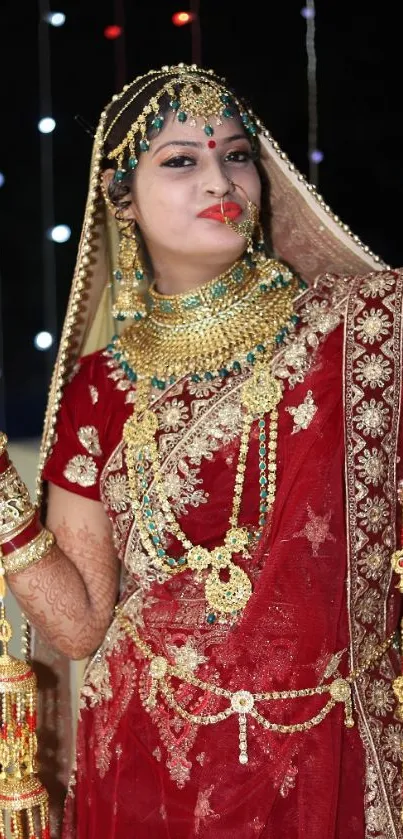 Bride in red saree with jewelry and festive lights.