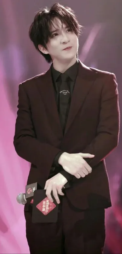 Elegant celebrity wearing a black suit on stage, surrounded by burgundy hues.