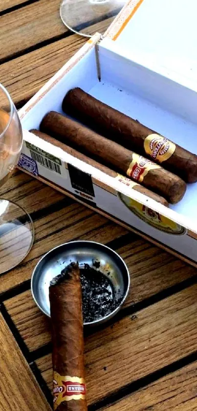 Cigars on a wooden table with whiskey and ashtray.