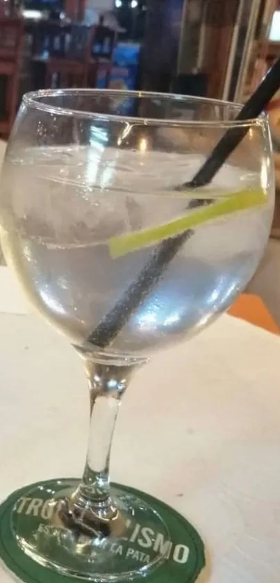 Cocktail glass with straw and lime on a table in a bar setting.