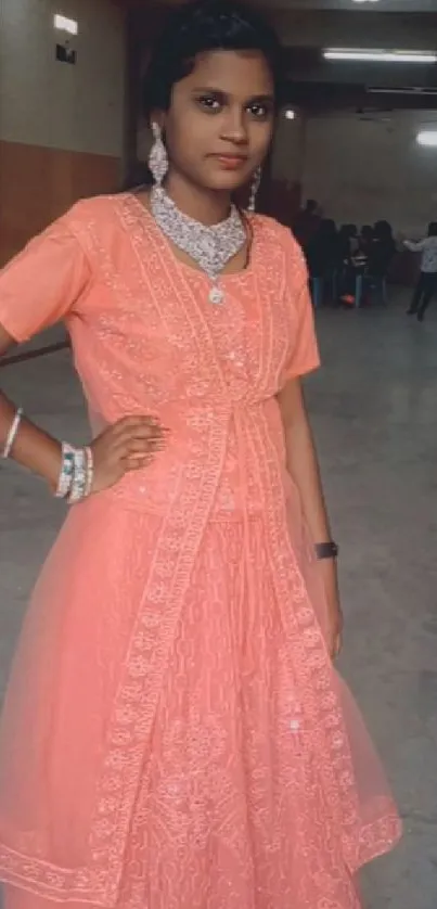 Elegant woman in coral dress standing indoors with intricate design details.